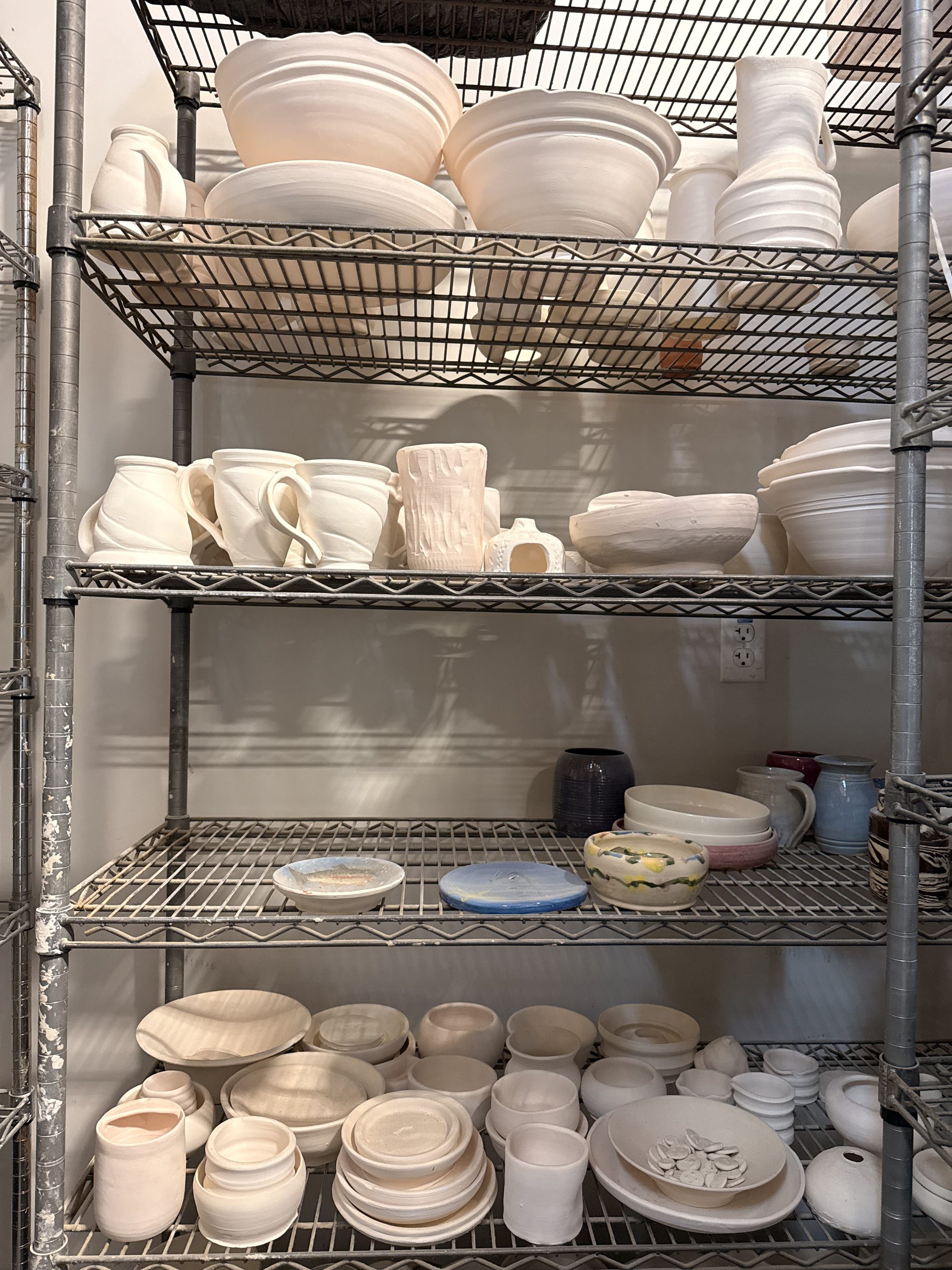 Shelves of bisque-fired mugs, bowls and plates waiting for glaze