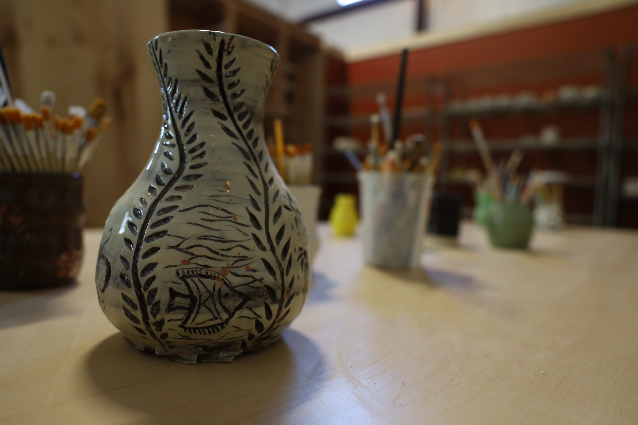 A carved vase with a fern and fish design on the studio table