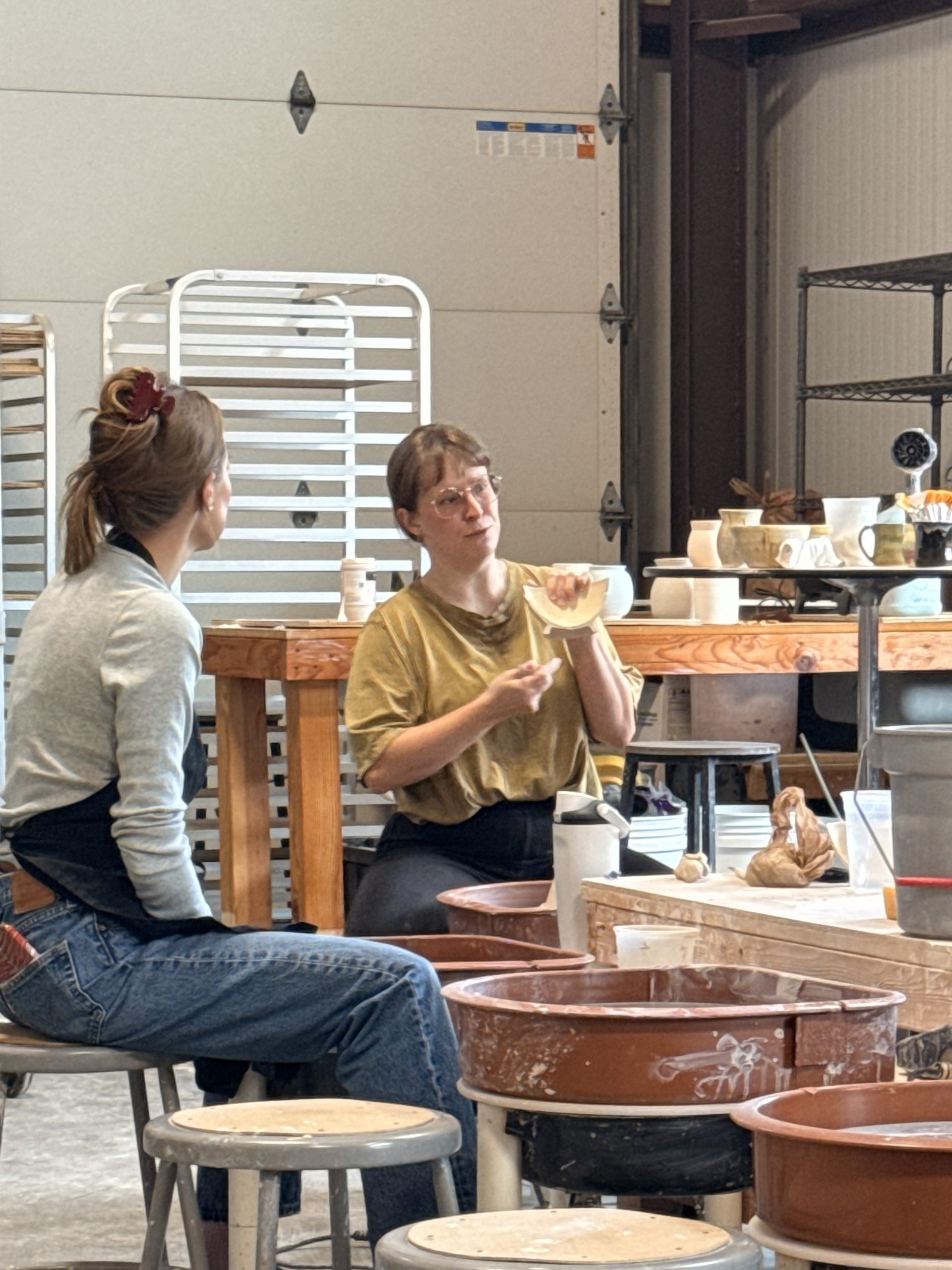 A potter talking a student through a piece at the wheels