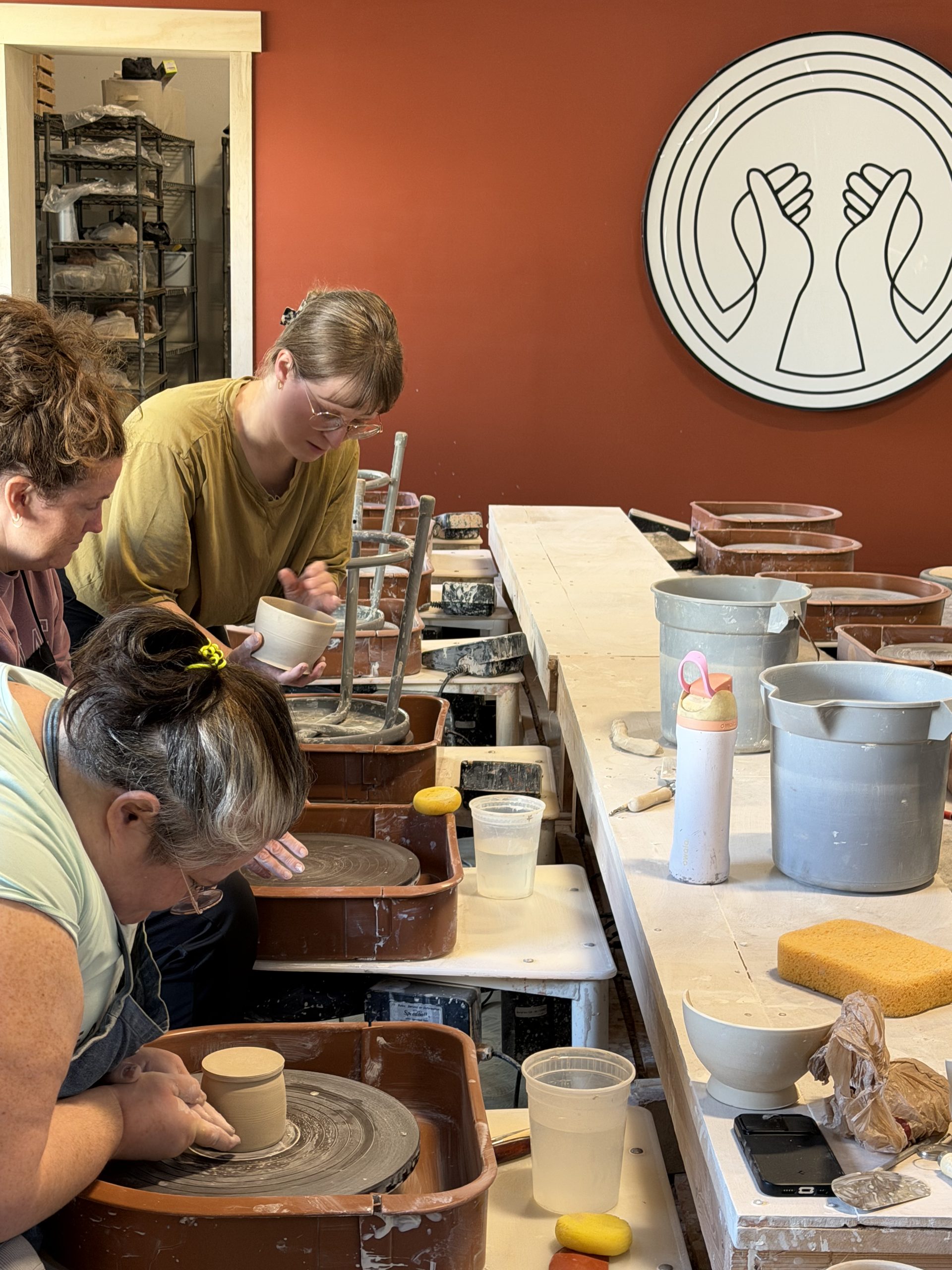 Students throwing at a row of wheels in front of the studio's logo wall